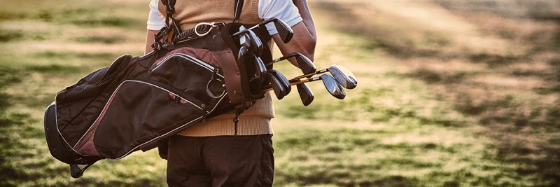 Man carrying golf bag while standing on field
